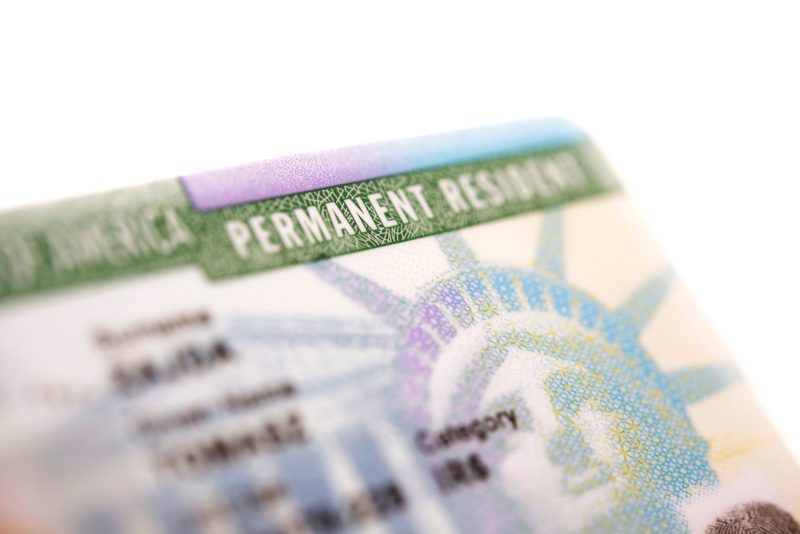 A close-up of a green card with the words "Permanent Resident" and the holder's information visible.