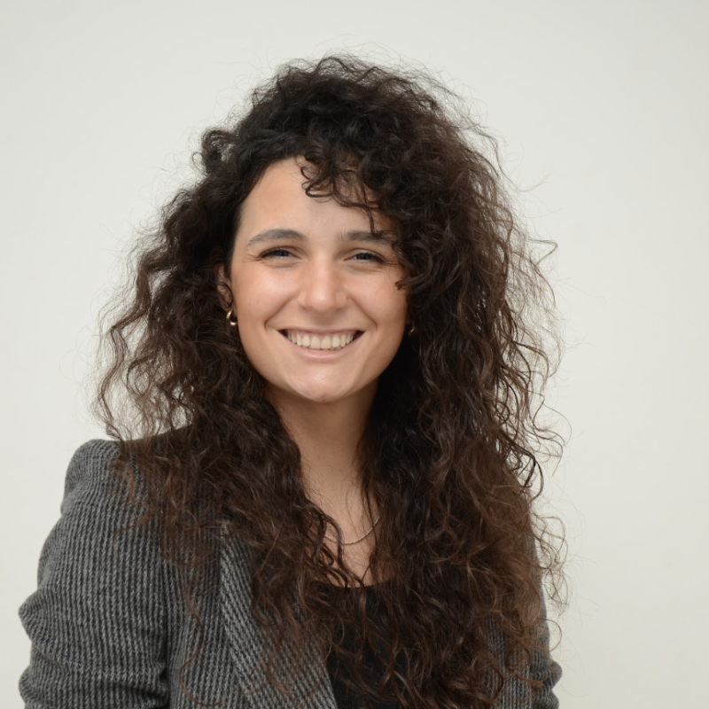 An image of Rafaela Serafini, a stylish woman with curly hair, wearing a suit jacket.