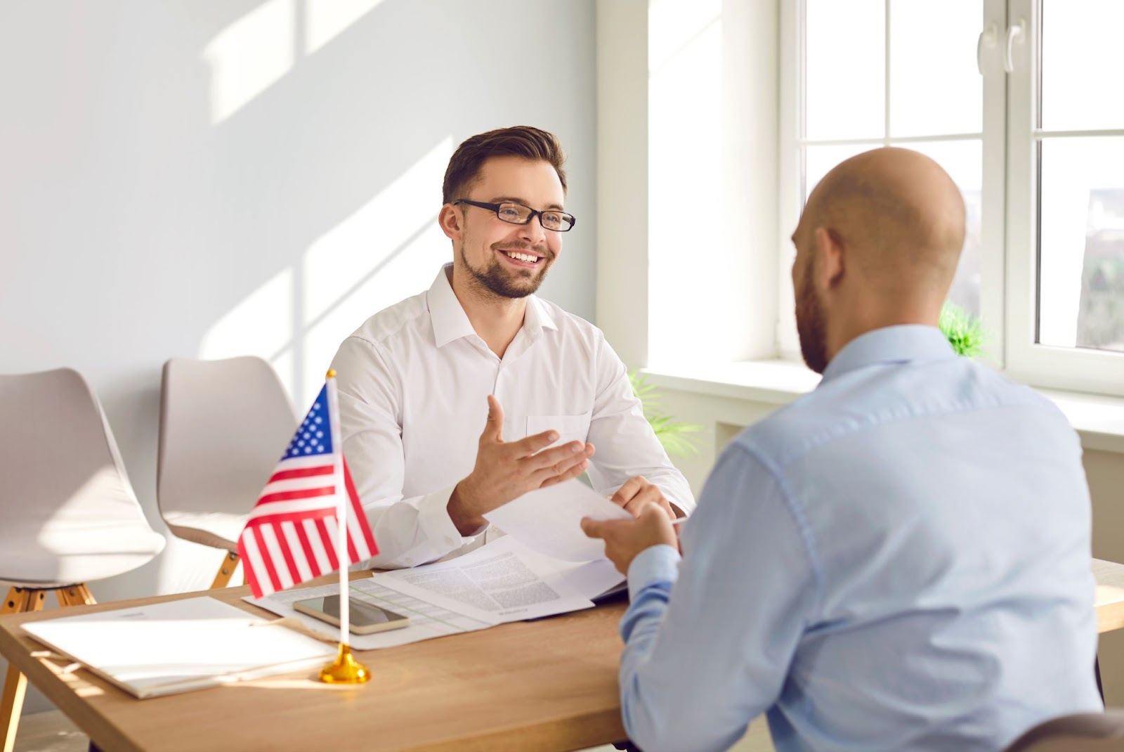 A man and woman sitting at a table with an American flag,discussing visa consultation and EB-1A Visa requirements.