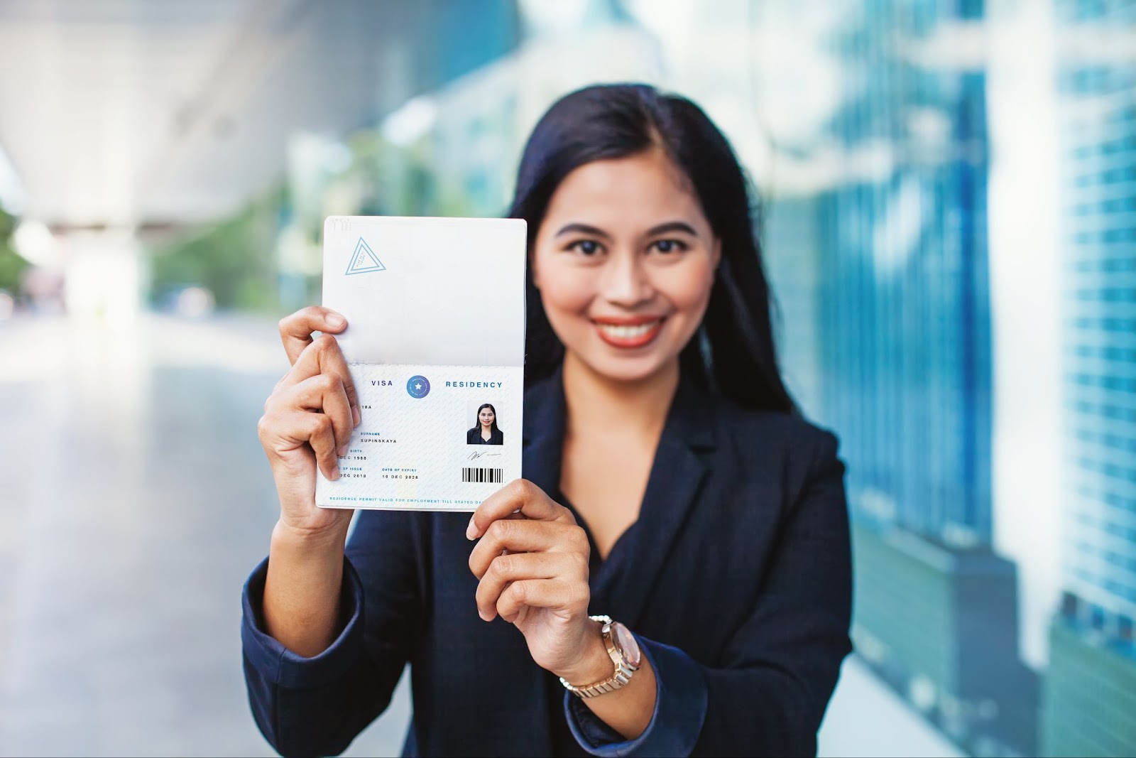 A professional woman in a business suit showcasing a card, possibly discussing visa consultation or EB-1A Visa requirements.