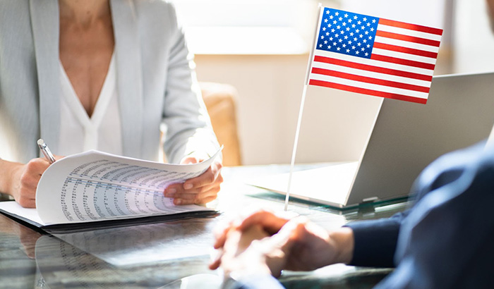 A man and woman sit at a table with a laptop and a flag. EB-2 immigration lawyer, US visa lawyer, EB-2 priority date.