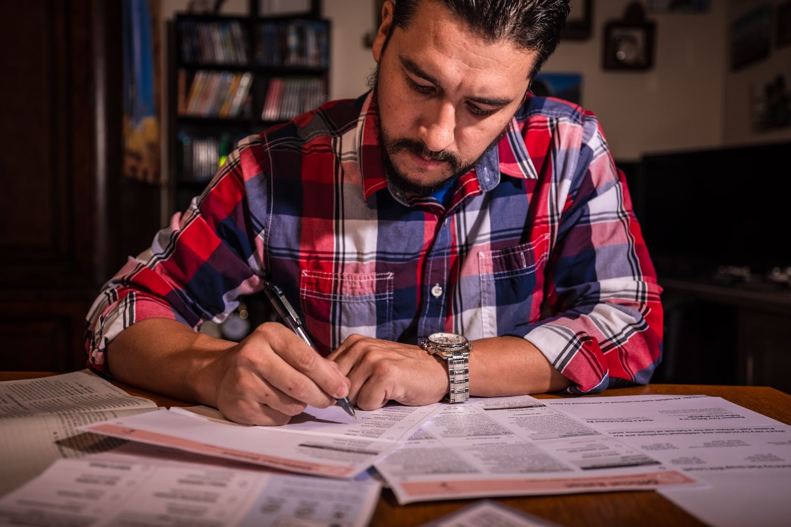 A man diligently writes on a paper at a table, reflecting on his journey to U.S. citizenship and the application process.